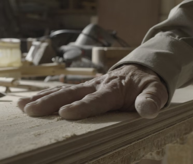 La mano del artesano apoyada sobre una tabla con fino aserrín, en el taller