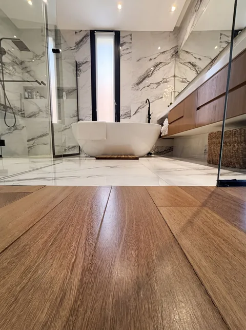 Baño con piso de madera, bañera exenta y mármol