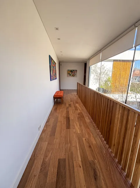 Pasillo con piso de madera, celosía de listones y banco naranja
