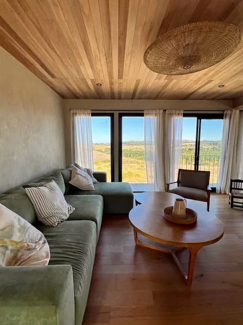 Living: sofá verde, mesa redonda de madera y vista a las sierras