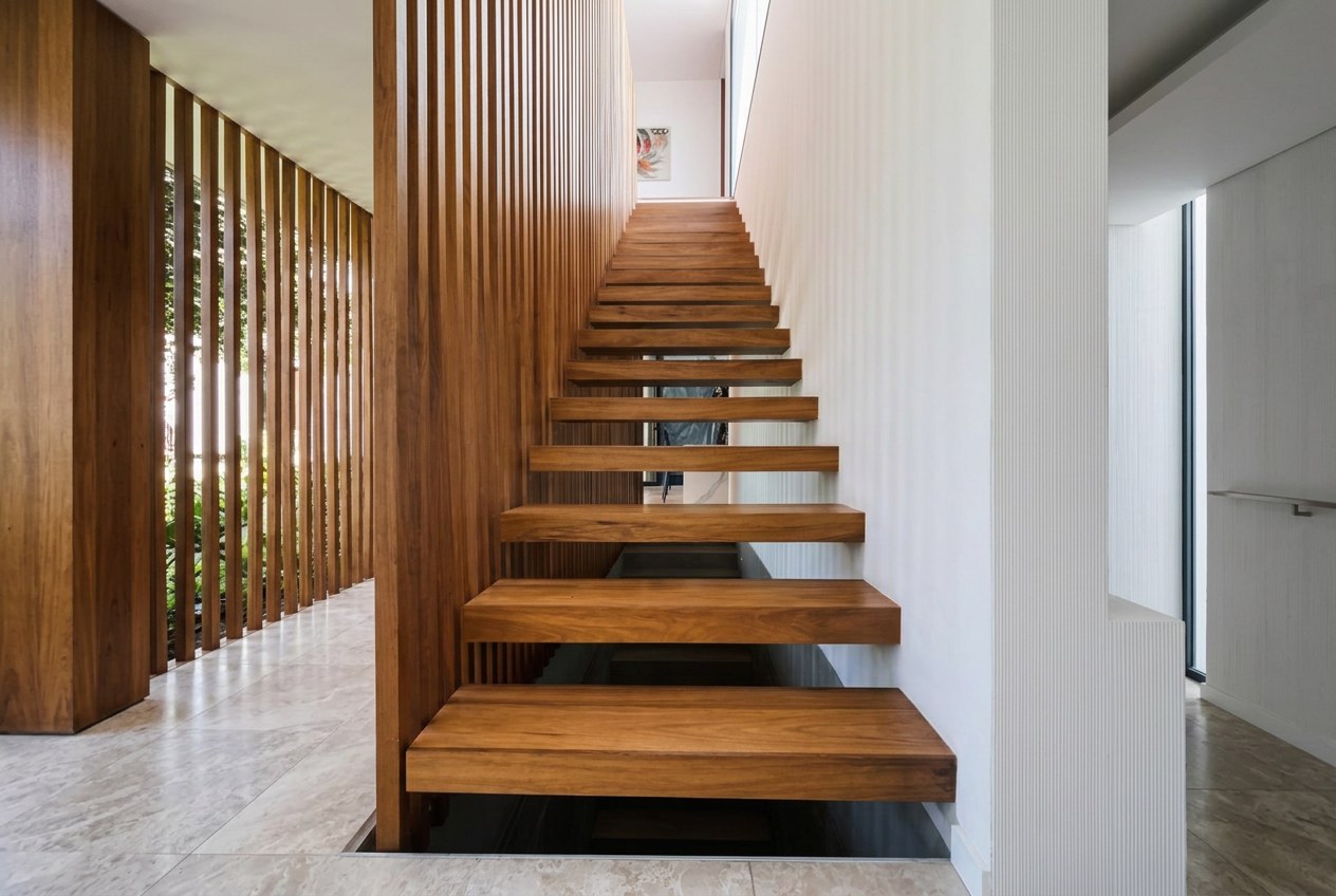 Escalera de escalones volados en madera maciza junto a un muro de listones